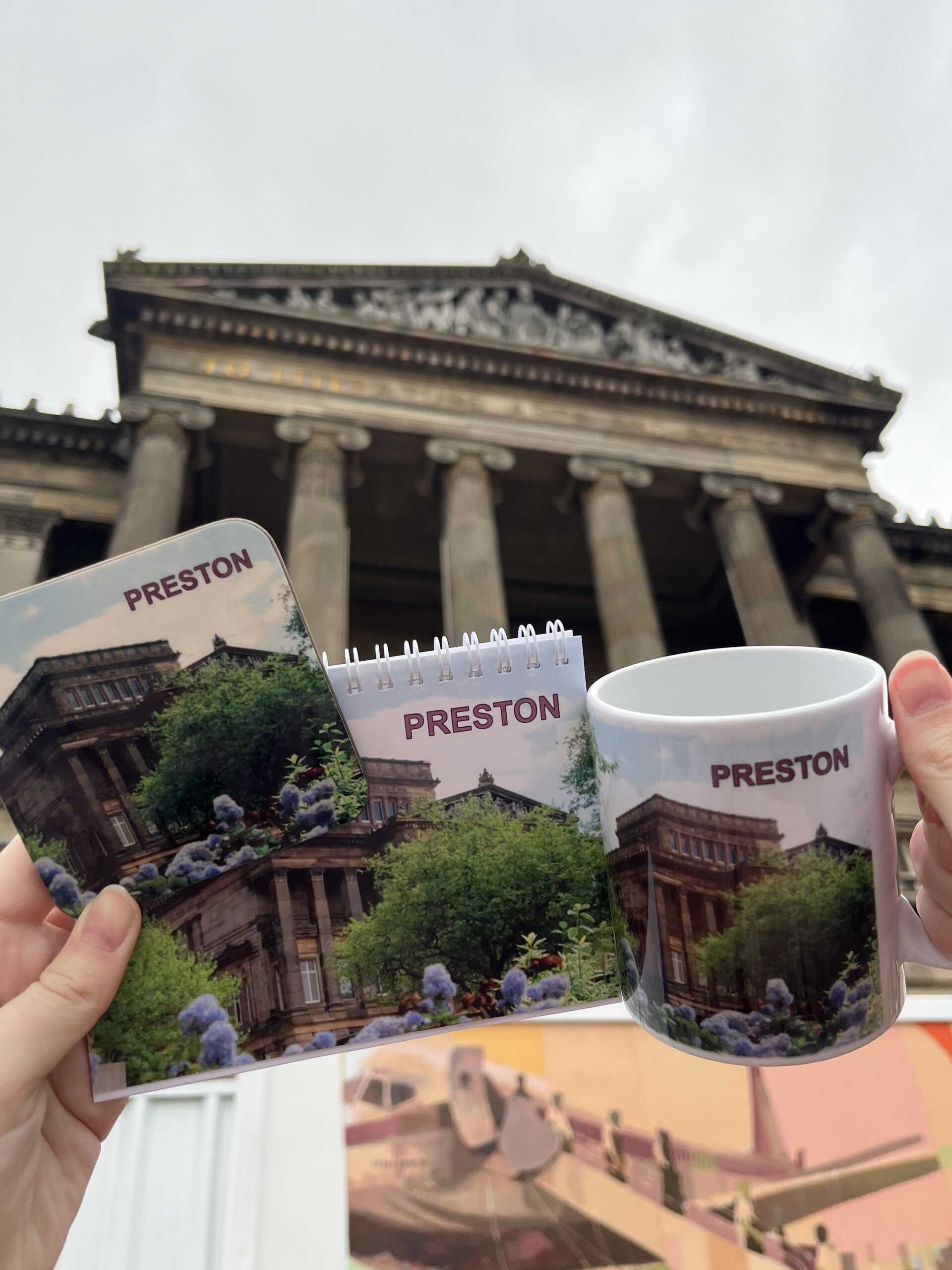 Image taken outside the Harris with Preston merchandise in the form of a mug, notepad and coaster.