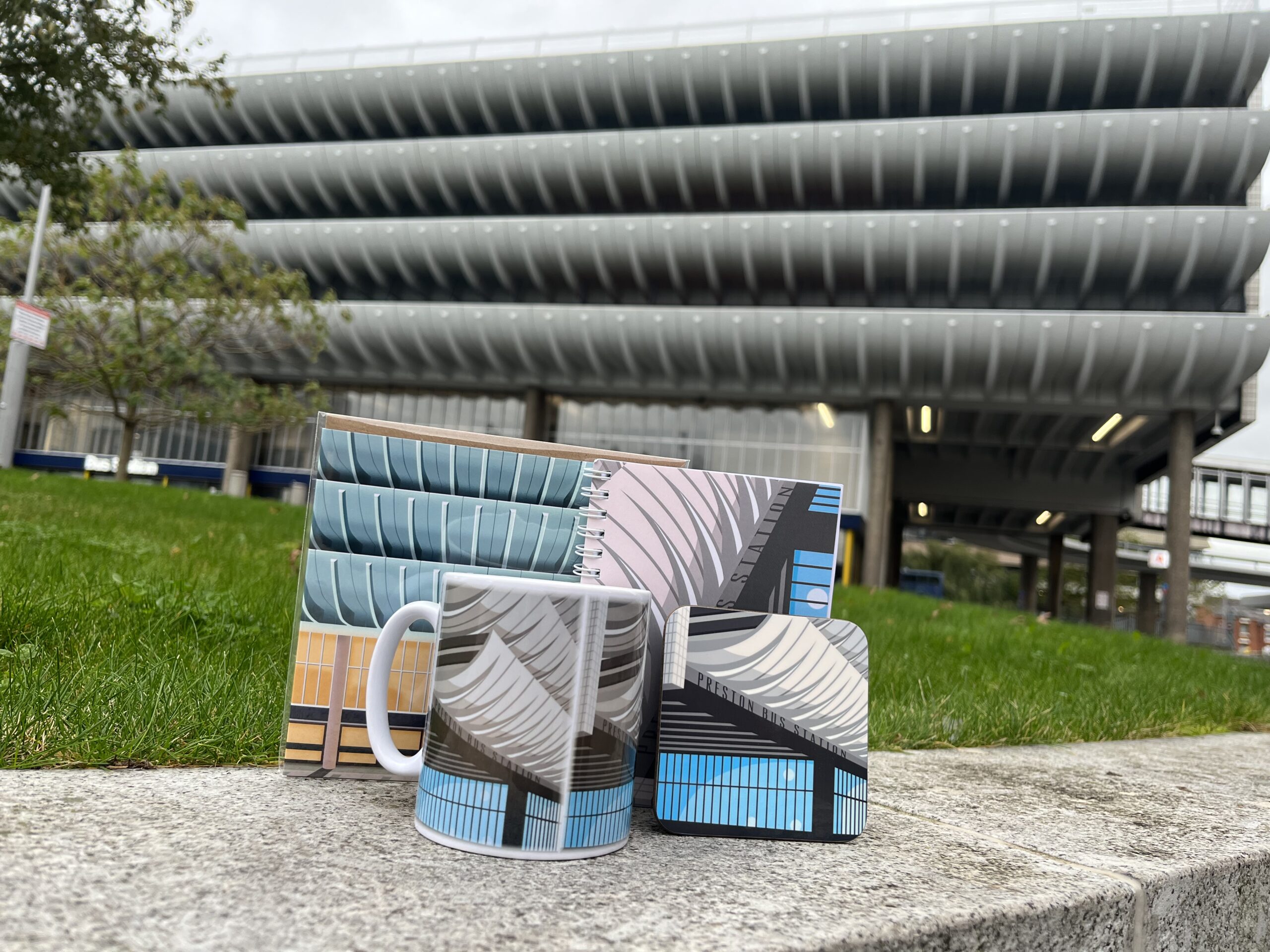 Preston bus station in the background with Preston bus station merchandise in the form of a mug, coaster and notebook.
