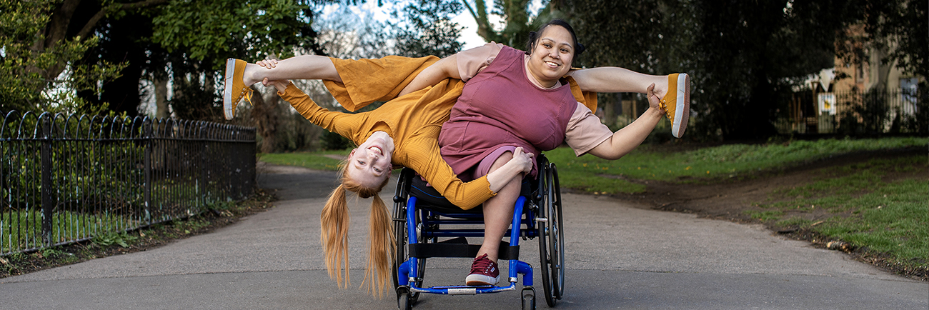 An image of a person in a wheelchair with another person upside down on their shoulder.