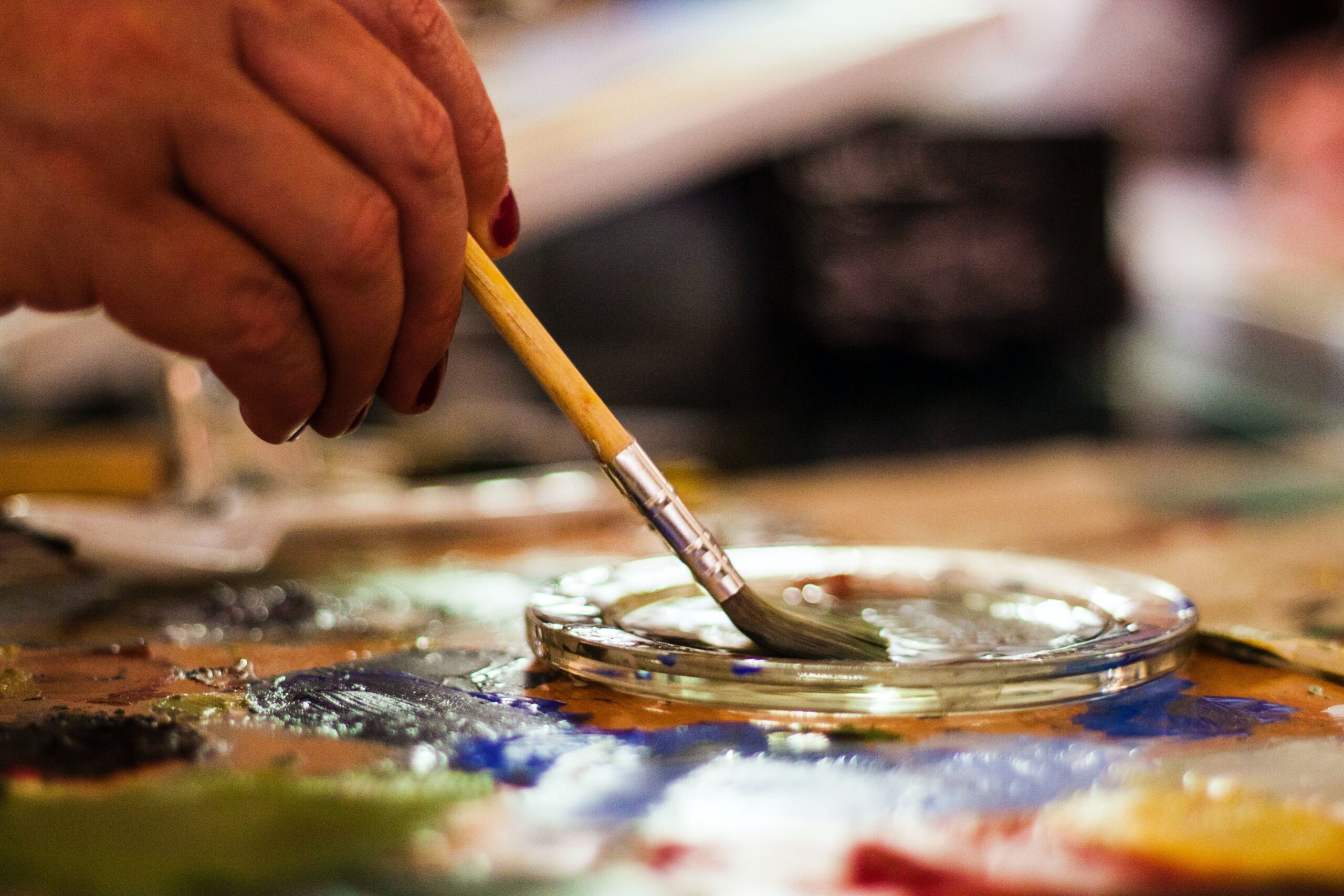 A person dips a paint brush into a glass tray.