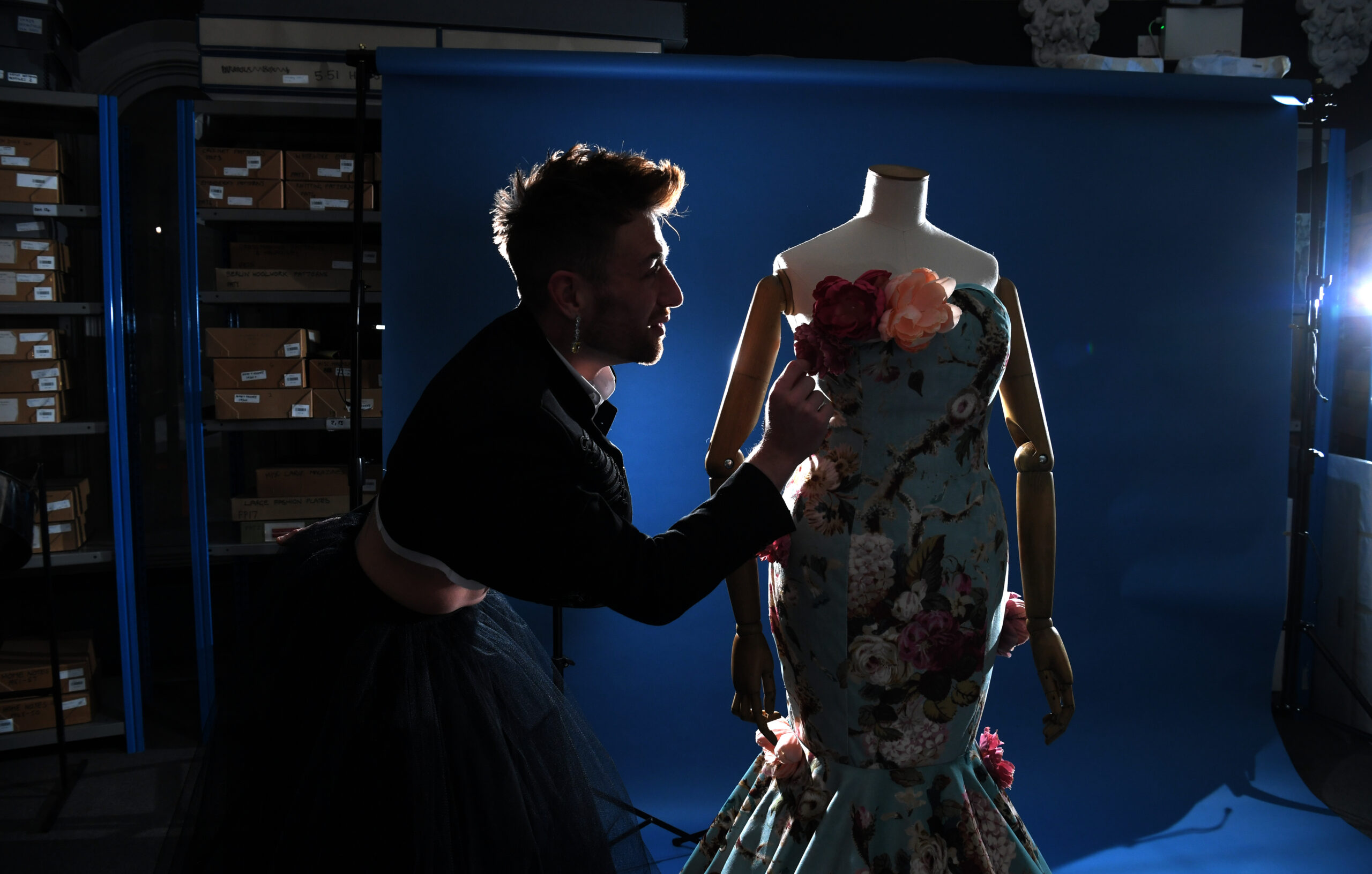 A person in a black jacket adjusts the roses decorating a blue dress.