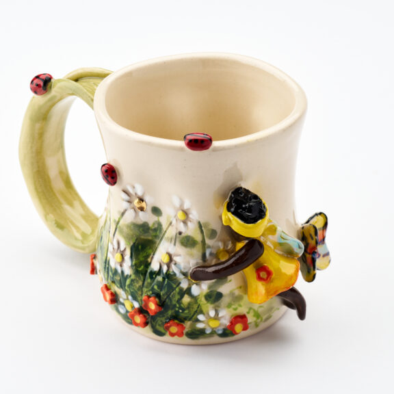 Image of a pottery work by Christine Cherry, a ceramic mug with bees and fairy embellishments.