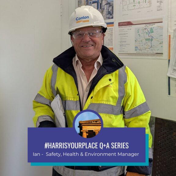 A person wearing a hard hat and protective clothing stands in an office.