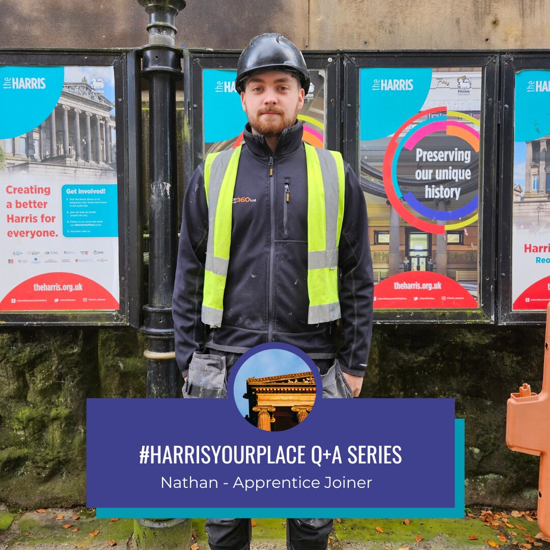 A person wearing a hard hat and protective clothing stands in front of colourful posters.