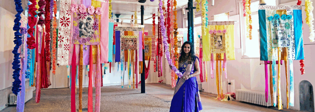 A person stood between colourful artwork hanging from the ceiling.
