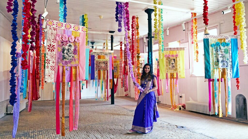 A person stood between colourful artwork hanging from the ceiling.