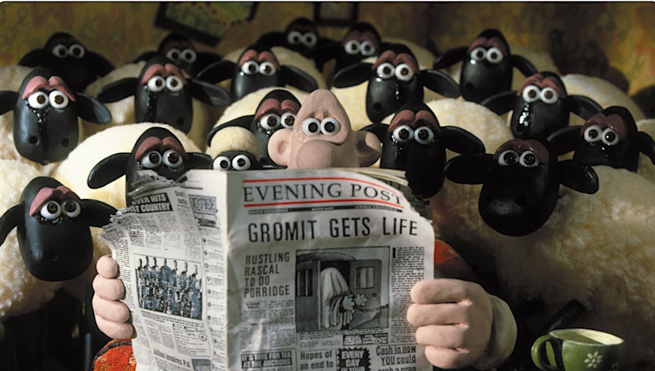 Wallace reads a newspaper surrounded by sheep.
