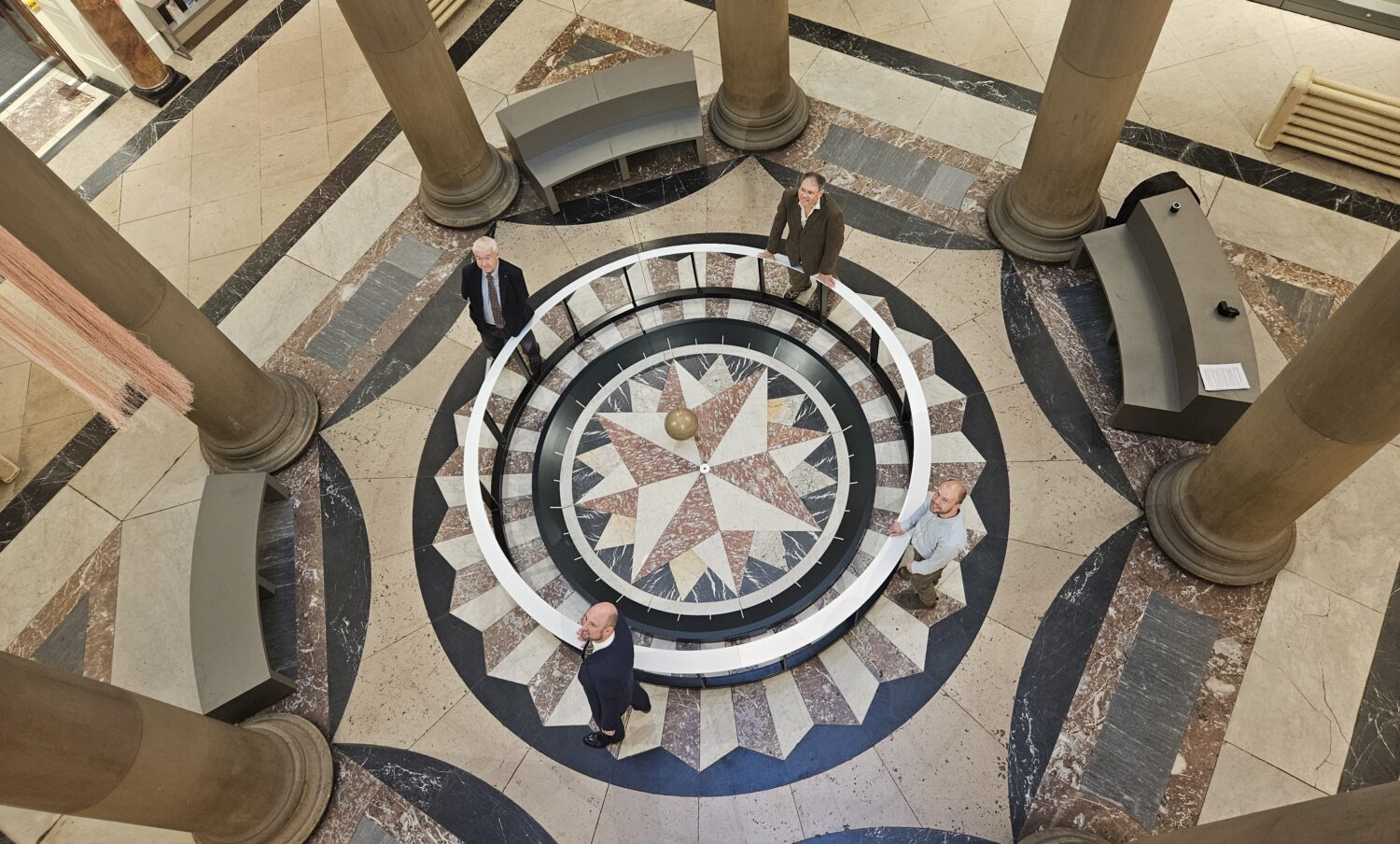 Four people stood around a pendulum base in the centre of a rotunda.
