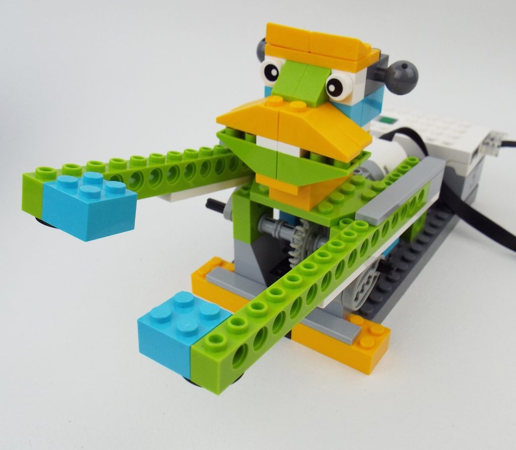 Colorful LEGO robot resembling a bird, with orange beak, green and light blue wings, and large eyes, conveying a playful, whimsical tone.