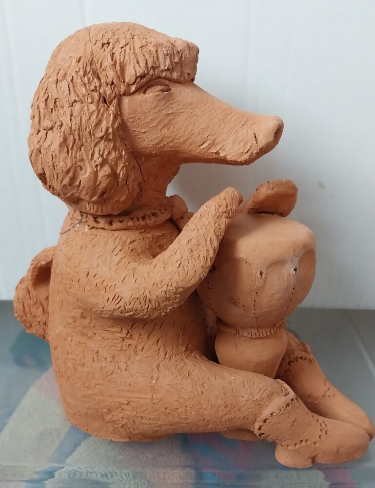 Clay sculpture of a seated poodle holding a smaller figure. The textured fur and gentle pose convey warmth and playfulness against a plain backdrop.