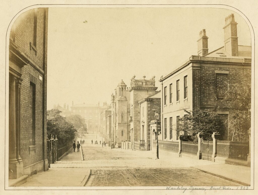 Historic sepia-toned photograph of an early 20th-century street with brick buildings, people walking on cobblestone road, and serene urban atmosphere.
