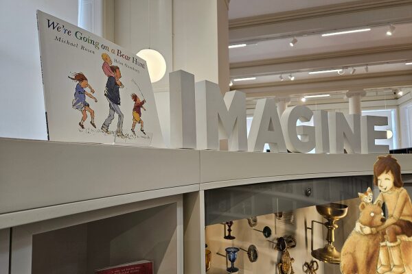 Children’s book, "We’re Going on a Bear Hunt," displayed on a shelf with the word "IMAGINE" in bold letters. Bright, inviting library setting.