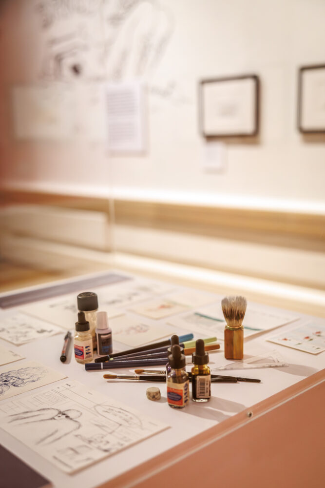Image of illustration tools including drawing matierials and ink in a glass display box.