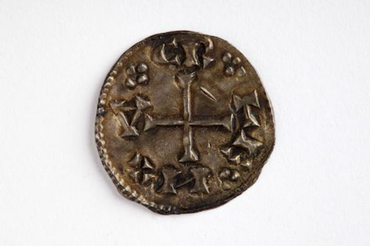 Ancient coin with a cross design centered, surrounded by small geometric shapes. The worn surface suggests historical significance and age.