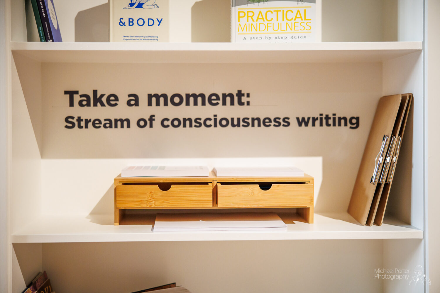 A shelf with books on mindfulness and writing tips. A sign reads, "Take a moment: Stream of consciousness writing," suggesting reflection and creativity.