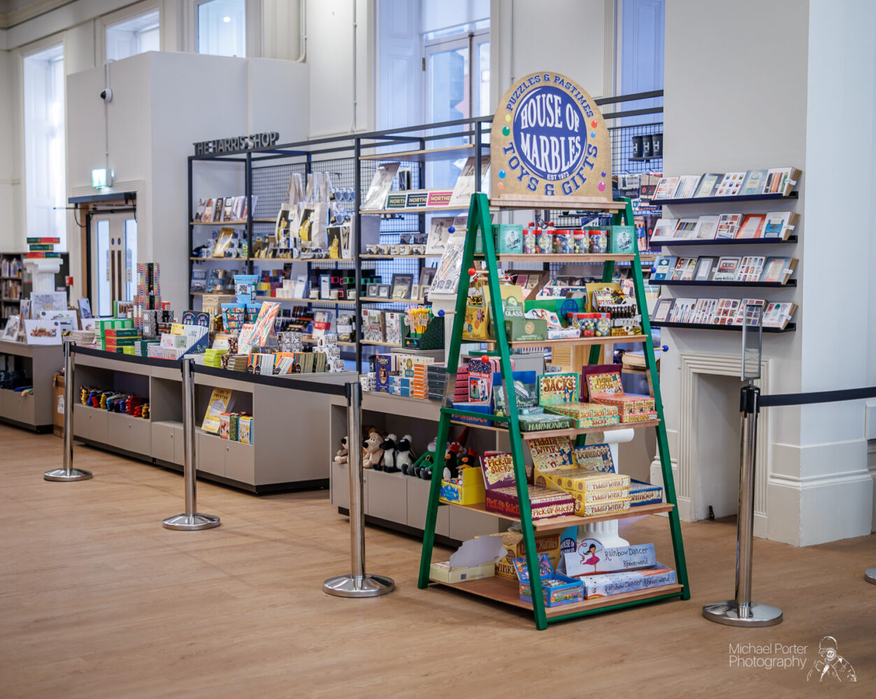 Spacious store interior with shelves displaying books, toys, and gifts. Prominent "House of Marbles" sign, bright and organized ambiance.
