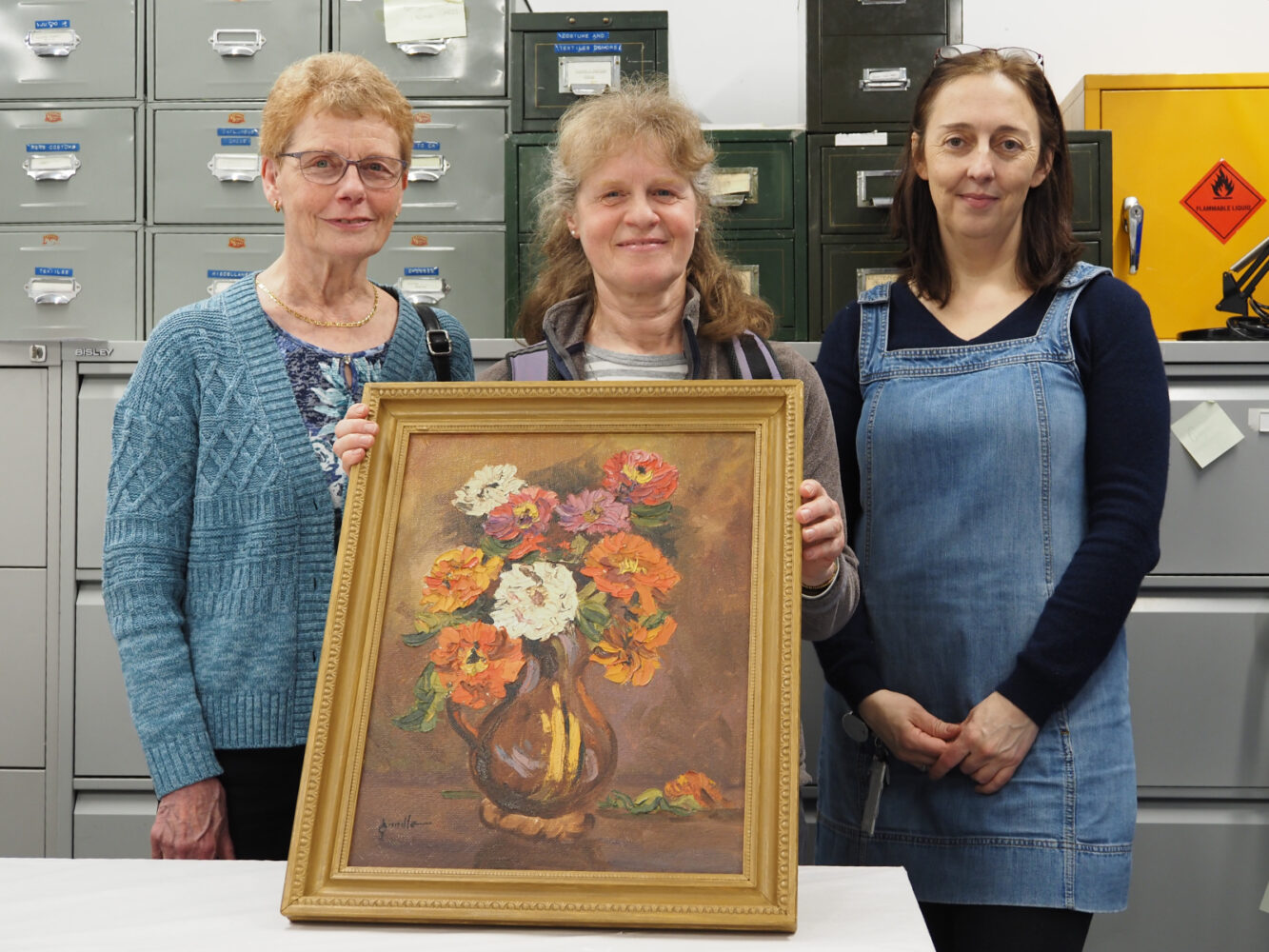Three people in an art store stand with a painting of flowers.