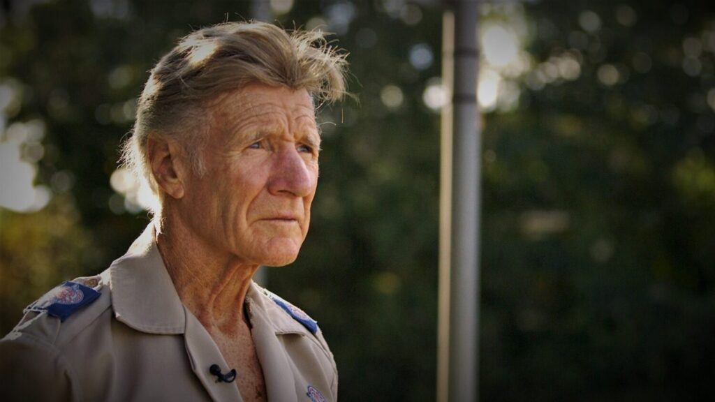 Image of a man in a grey uniform looking past the camera.