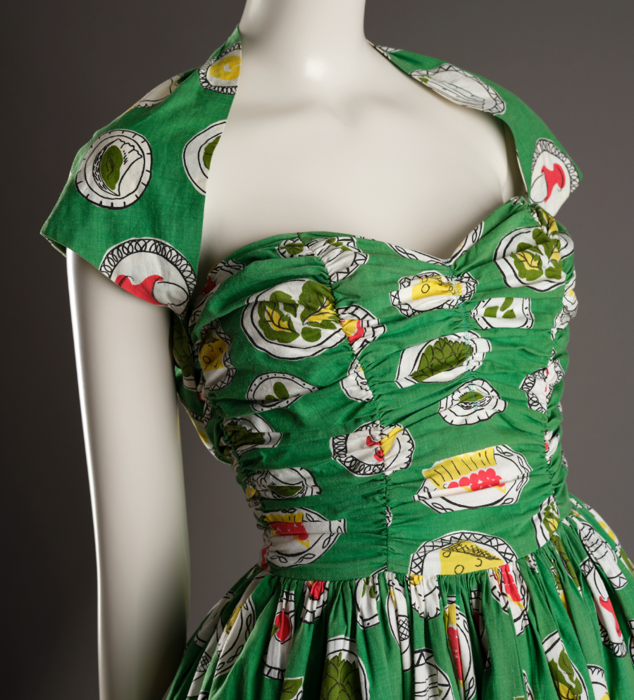 Image of a mannequin with a green dress covered with a bright pattern of plates including dishes.