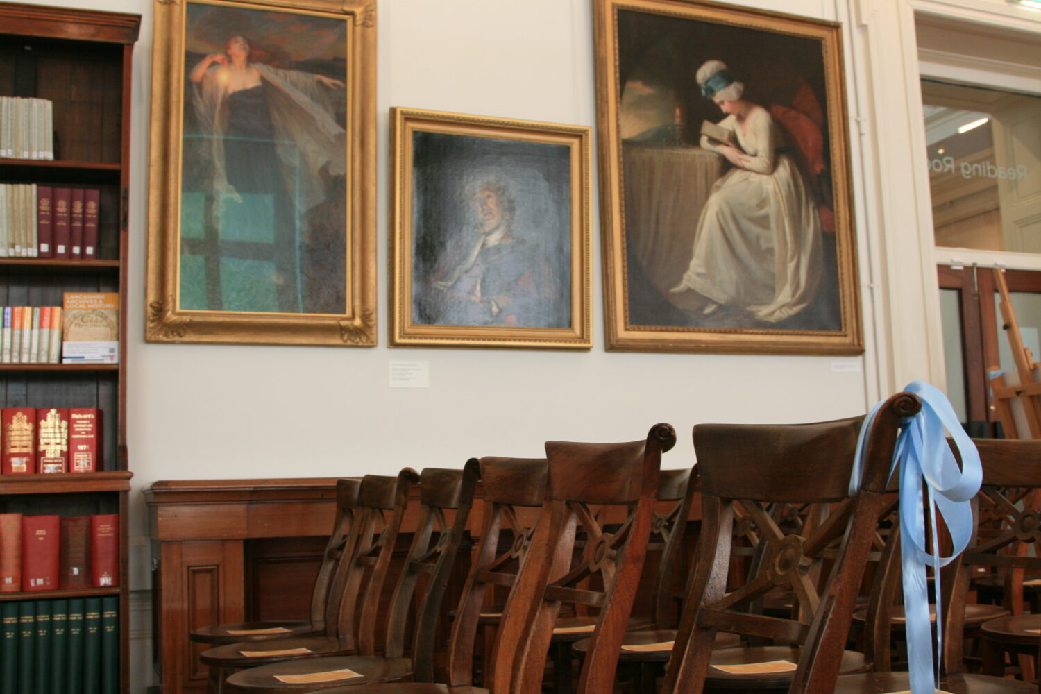 Image of brown chairs in a line with a baby blue bow tied on one chair.