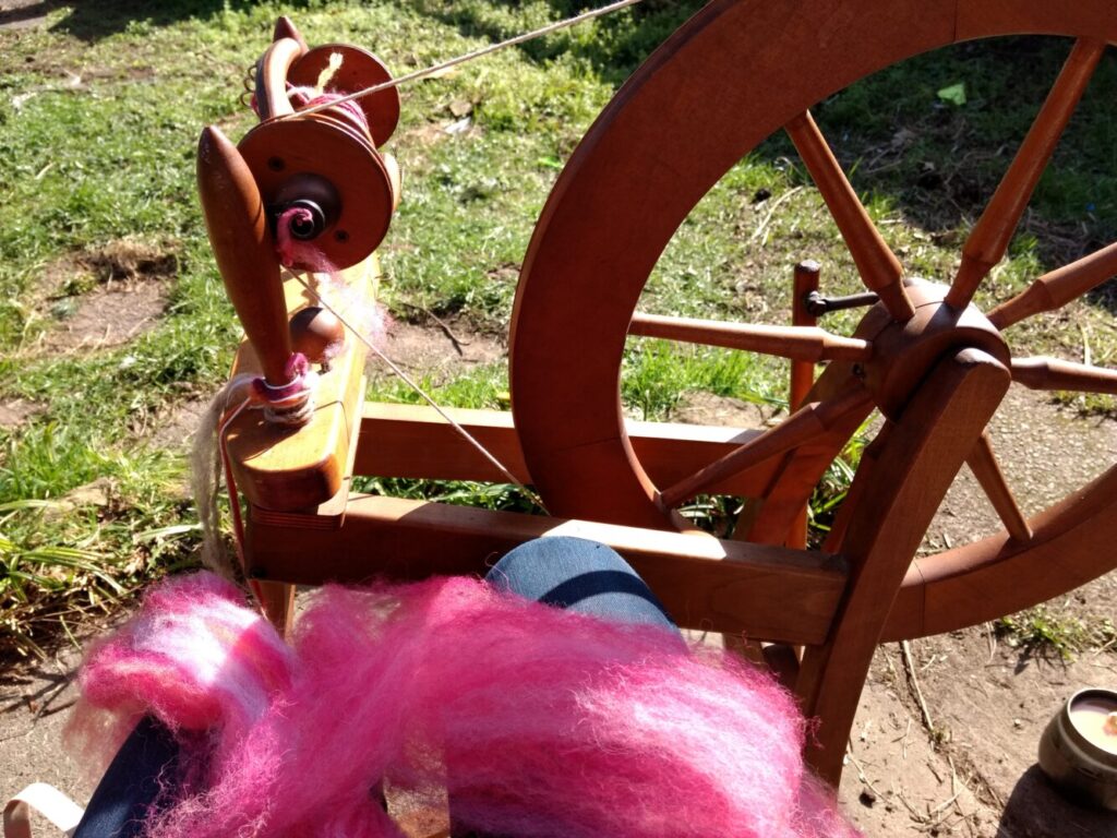Image of a wooden spinning wheel with bright pink cotton.