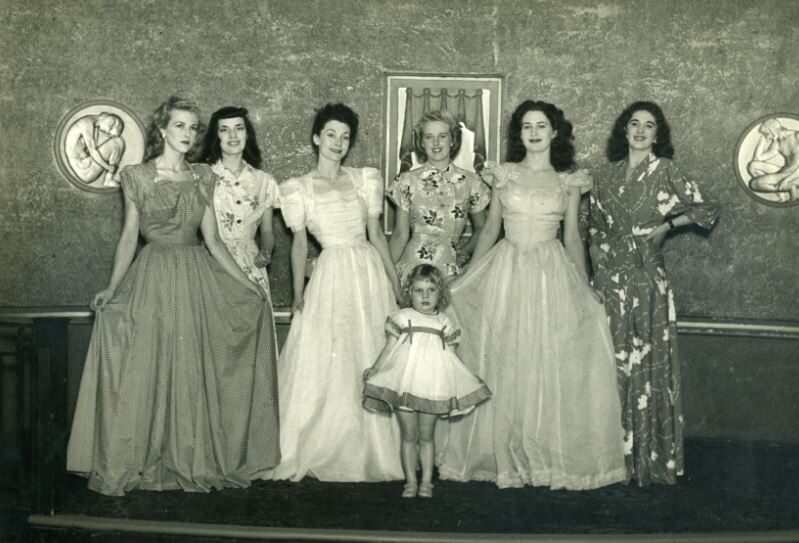 Image of seven people wearing dresses stood in a lin posing or a picture.