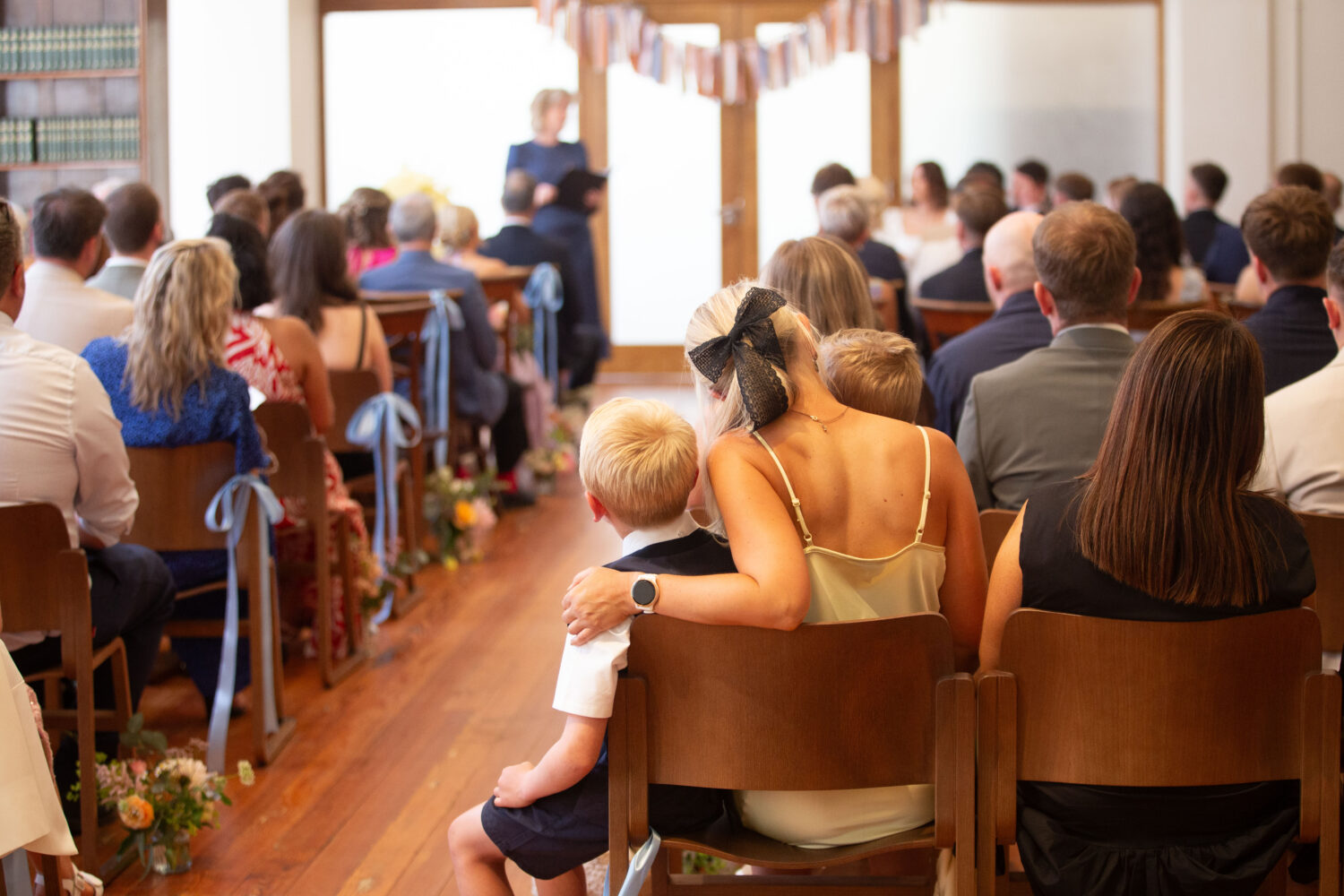 Image of a wedding party seated on wooden chairs.