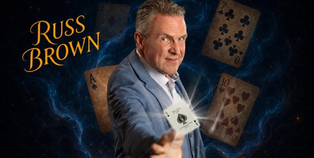 Image of a magician wearing a smart blue suit with playing cards in the background.