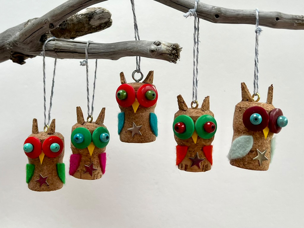 Cork crafts of owls with different rainbow coloured eyes hanging from a tree branch.